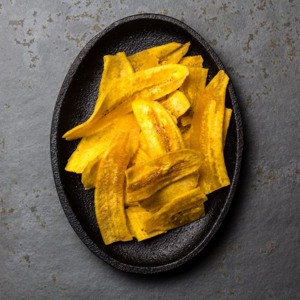 Healthy Homemade banana Plantain Chips on black plate, slate background